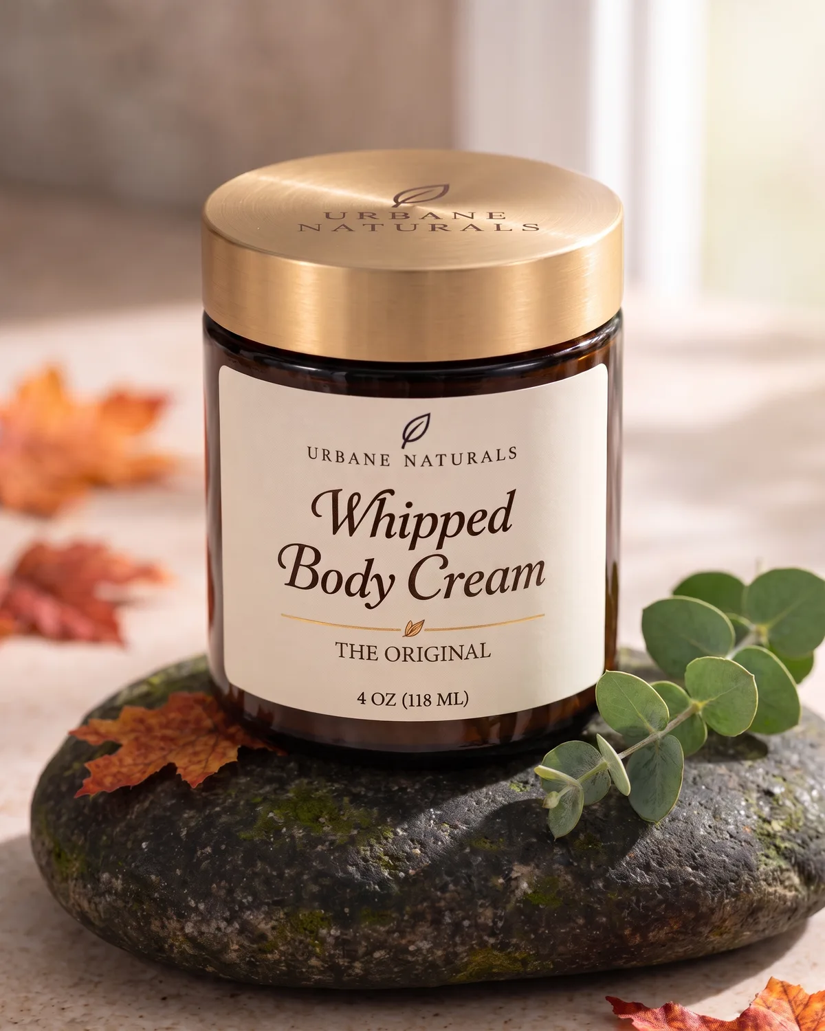 Closed amber glass jar of Whipped Body Cream with an engraved gold lid on a mossy stone